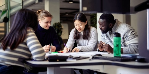 International students studying/chatting together in the Stack Room in Queen's Building Library. A mix of genders and study levels completing group work.